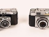 two old cameras sitting side by side on a white surface