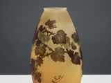 a yellow vase with leaves on it sitting on a table