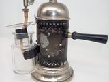 a silver coffee grinder with a glass on a white table