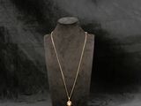 un collier en or posé sur un présentoir à mannequin, sur fond noir