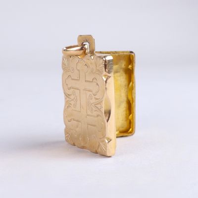 un pendentif en or orné d'une croix, posé sur un fond blanc