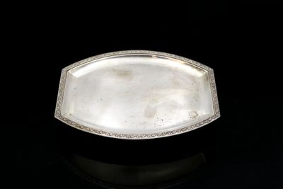 an antique silver plate with a decorative edge on a black surface
