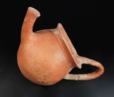 un petit vase marron muni d'une anse, posé sur un fond noir