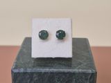 une paire de boucles d'oreilles en jade vert posées sur un bloc de marbre