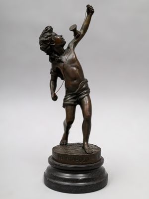 une statue antique en bronze représentant un garçon tenant une raquette de tennis