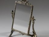 un miroir ancien plaqué argent, posé sur un pied et orné d'un oiseau