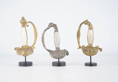 trois figurines en argent et en or posées sur des socles, sur une surface blanche