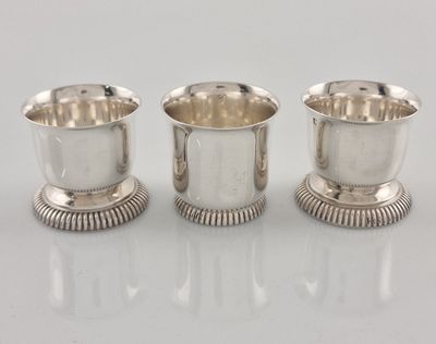 trois tasses en métal argenté sont alignées sur une surface blanche