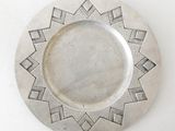 a silver plate with geometric designs on it on a white surface