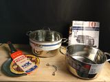 plusieurs casseroles et poêles posées sur une planche à découper en bois, à côté d'un livre de cuisine