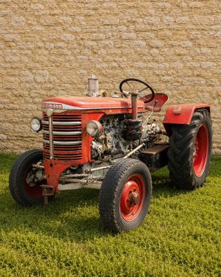 un tracteur rouge garé dans l'herbe près d'un mur de briques
