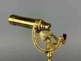 an antique brass telescope on a stand against a gray background