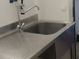 un évier en inox dans une cuisine, avec un réfrigérateur en arrière-plan