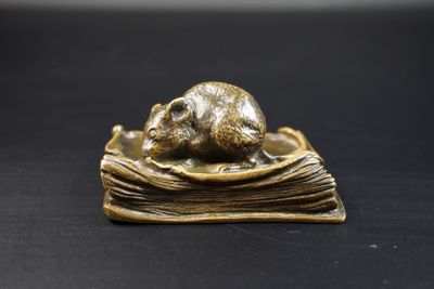 figurine en bronze représentant une souris posée sur un livre, sur un fond noir