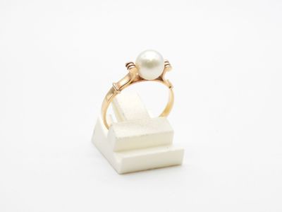 une bague en perle et en or posée sur un bloc de marbre blanc