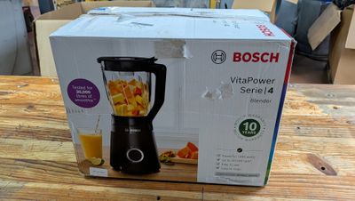 boîte contenant un mixeur, posée sur une table, avec un verre de jus d'orange à l'intérieur