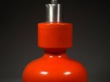 an orange vase with a silver top sitting on a gray surface