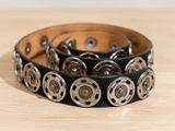 bracelet en cuir noir orné de clous métalliques sur un support en bois