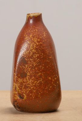 un vase marron posé sur une table en bois, près d'un mur blanc