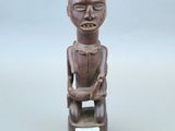 statue en bois représentant un homme assis sur un tabouret, tenant une étiquette à la main