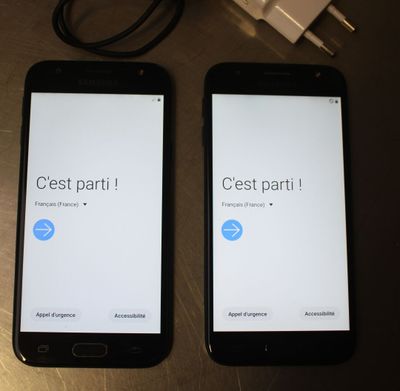 two cell phones sitting on top of a wooden table next to a charger
