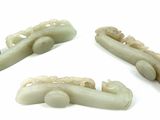 three pieces of white jade carved hair clips on a white surface