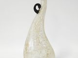 un vase en verre muni d'une anse noire, posé sur une surface blanche