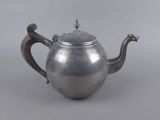 an antique silver teapot with a bird handle on a grey background
