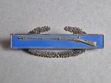 a blue and silver badge with a rifle on it