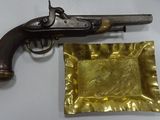 un vieux pistolet et une assiette en or posée sur une table blanche