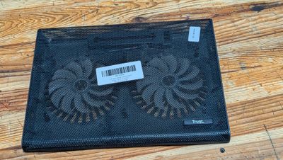 un ordinateur portable posé sur un support de refroidissement, lui-même posé sur une table en bois