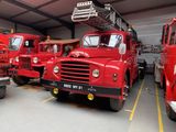 three red fire trucks are parked in a garage with a ladder