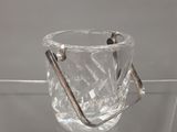 un vase en verre transparent muni d'une poignée en métal, posé sur une étagère en verre