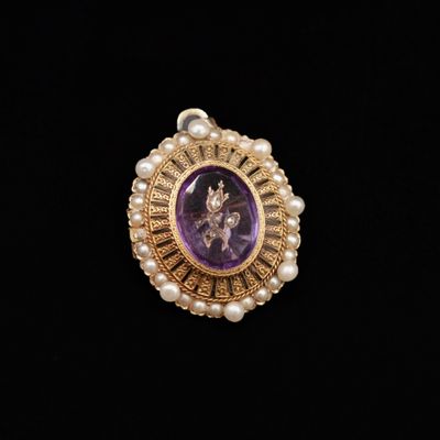 a close up of a purple stone and pearl broochle on a black background