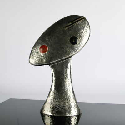 sculpture en argent représentant un poisson à l'œil rouge posé sur une surface noire