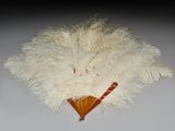 un éventail en plumes blanches avec un manche en bois posé sur une table
