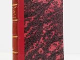an old book with a red cover sitting on top of a white table