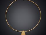 a gold necklace with a tear shaped stone on a black background