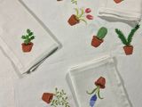 des serviettes brodées représentant des plantes en pot, posées sur une table