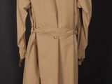 a tan trench coat on a mannequin stand against a black background
