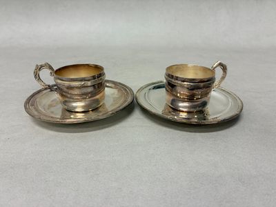 two silver plated cups and saucers on a white surface