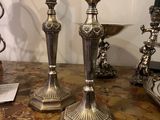 two silver candlesticks on a table with a picture on the wall in the background