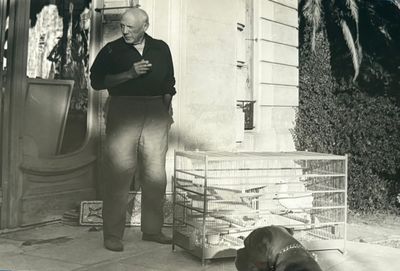 black and white photo of a man standing in front of a house with a dog