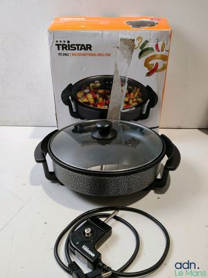 Une poêle électrique est posée sur une table, à côté d'une boîte de provisions.