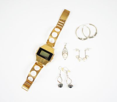 une montre en or et une paire de boucles d'oreilles posées sur une surface blanche