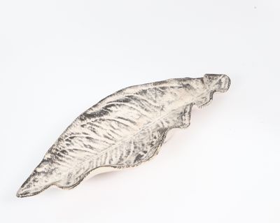leaf shaped metal object on a white surface with a white background