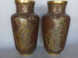 deux vases marron ornés de motifs dorés, posés sur une surface blanche