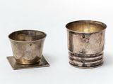 a silver cup and saucer sitting on a white surface