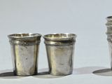 trois verres à shot en argent posés les uns à côté des autres sur une surface blanche
