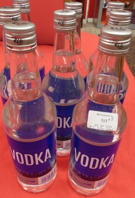 Six bouteilles de vodka sont alignées sur une table rouge.
